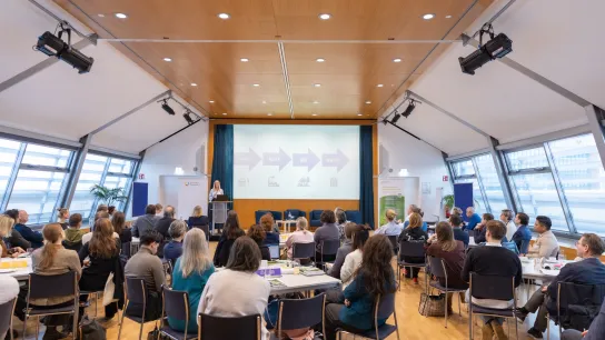© Monika Fellner / Gesundheit Österreich Teilnehmende sitzen im Konferenzsaal und verfolgen einen Vortrag zur Kreislaufwirtschaft im Gesundheitswesen auf der Bühne.