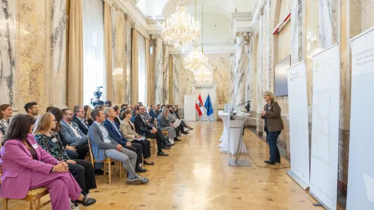 (ns)© Monika Fellner / Gesundheit Österreich Podiumsdiskussion beim Best Practice Award „Klimafreundliche Gesundheitseinrichtungen“ 2026. Fünf Personen diskutieren an Stehtischen vor einem sitzenden Publikum im Festsaal des Gesundheitsministeriums. Eine Teilnehmerin spricht ins Mikrofon, die Diskussion wird gefilmt.